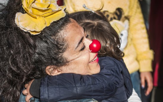 En clown i röd näsa blir omkramad av ett barn